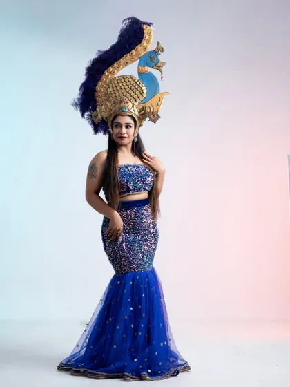 A full-length view of the blue sequin gown and peacock headpiece, a perfect combination for a fantasy or themed event.