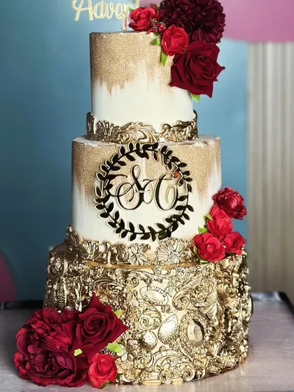 Love is in the details. This golden and red wedding cake radiates warmth and regal charm, featuring a dramatic gold-leafed bottom tier and crowned with rich red sugar roses.