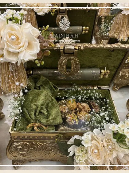 An olive green Rajwada chest filled with gourmet treats in a velvet potli and other treasures. I offer a wide range of products to curate the perfect gift for any occasion within this collection.