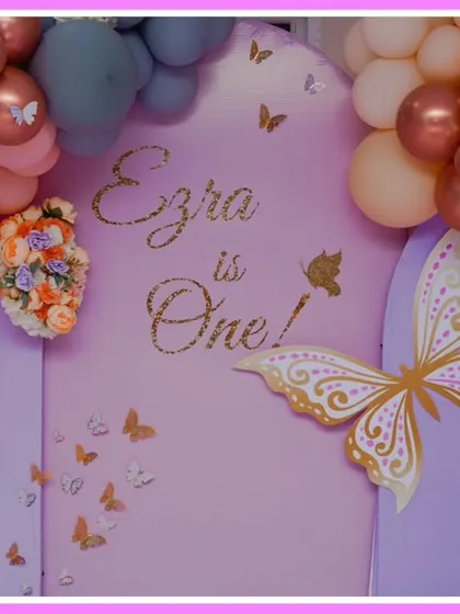 A close-up of a butterfly-themed first birthday backdrop. The soft peach and purple color palette and elegant butterfly graphics create a sophisticated look.