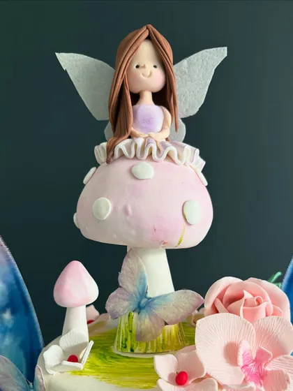 A whimsical fairyland on a cake. This two-tiered creation features a delightful fairy perched on a mushroom, surrounded by wafer-paper butterflies and handcrafted sugar flowers for a 5th birthday.
