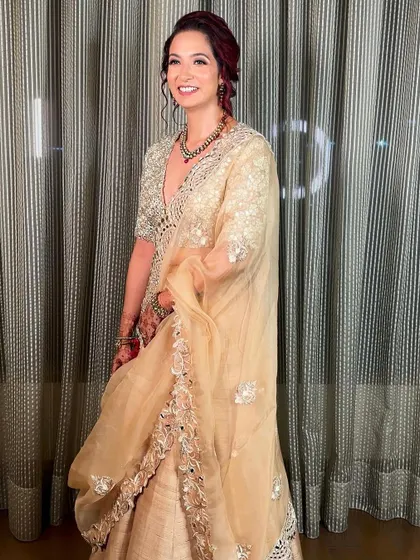 A full-length view of her beautiful beige and mirror-work outfit. The soft, radiant makeup ensures she looks put-together and elegant without being overdone.