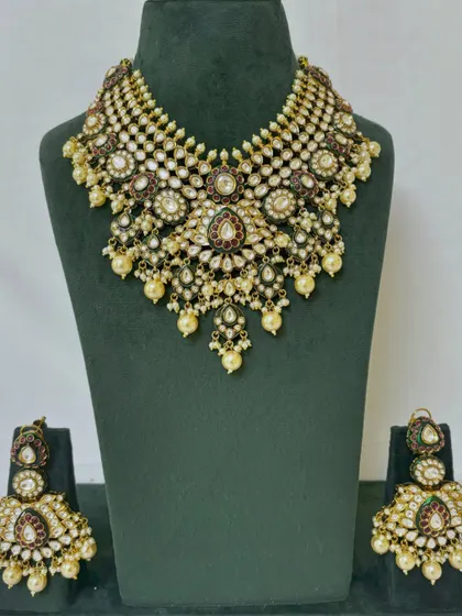 This rental choker set is adorned with small pearls and red and green stones. It comes with matching oversized earrings.