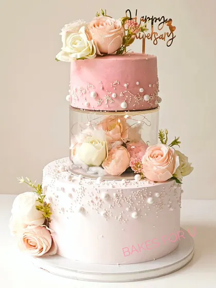 Celebrating 30 years of love with this stunning Pearl Anniversary cake. This three-tier design features a clear separator filled with fresh flowers and lights, surrounded by delicate pearl details.