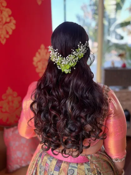 A soft and romantic half-updo with beautiful curls. The hair is adorned with a crown of fresh green and white flowers for a natural, organic feel.