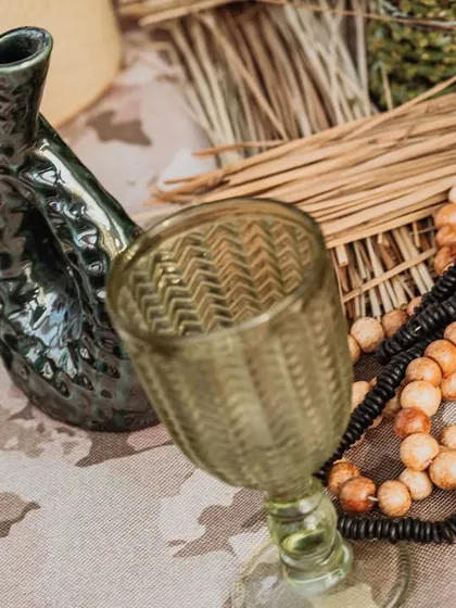 A close-up of the tabletop decor, featuring unique black ceramic vases, a textured green glass, and wooden beads. The details are rustic, earthy, and perfectly on-theme.