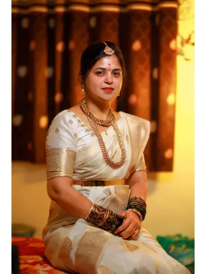 A regal portrait of the bride seated, dressed in an elegant white and gold saree.