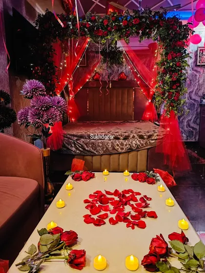 This image focuses on the small details that make the setup special. A table is decorated with scattered red rose petals and surrounded by warm, flickering battery-operated candles for a safe and romantic ambiance.
