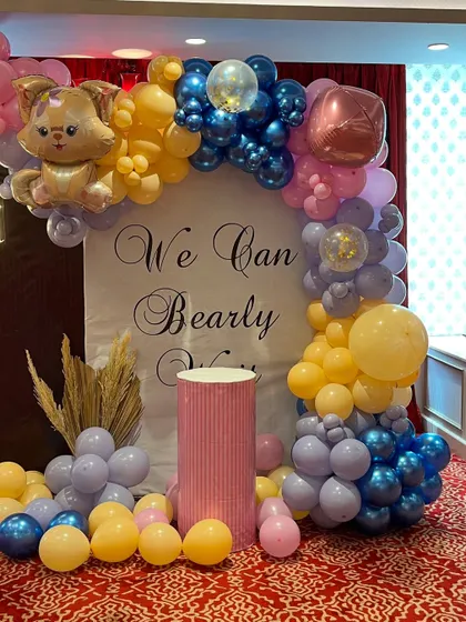 A detail shot of the baby shower backdrop, featuring a cute cat foil balloon and a mix of blue, yellow, and purple balloons. The pedestal is ready for the cake.