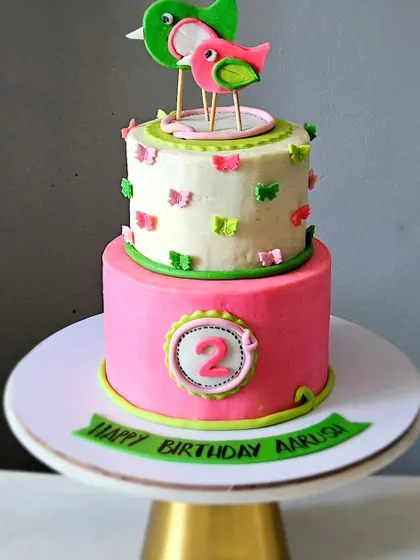 A slightly different angle of the cute two-tier birdie cake, showcasing its bright pink and green colors.