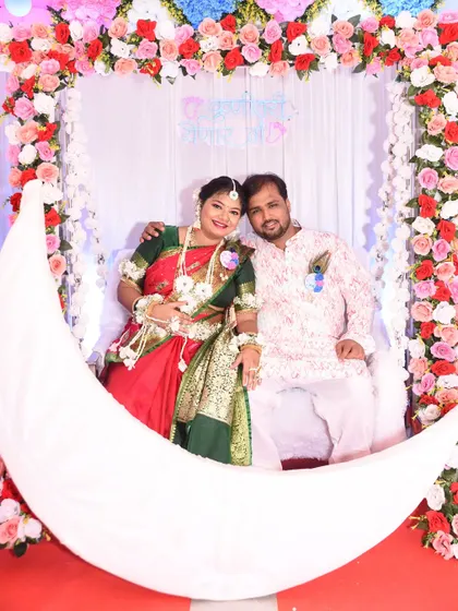 A lovely photo of the couple seated on a crescent moon prop at their baby shower, surrounded by a vibrant floral arch.