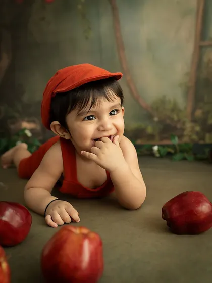 A moment of discovery. This baby is tasting his fingers, a classic milestone, while surrounded by bright red apples.