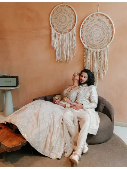 A stylish, relaxed portrait of the couple lounging together, showcasing their modern wedding attire and the bohemian decor.