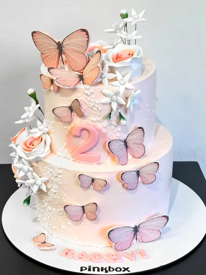 This delicate two-tiered cake is adorned with beautiful, lifelike butterflies, creating a whimsical and elegant look for a second birthday or any spring-themed celebration.