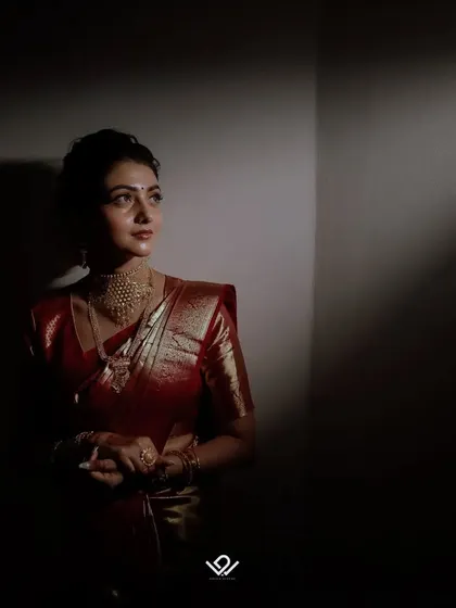 A bridal portrait using dramatic lighting to create a chiaroscuro effect, highlighting the bride's features and red saree.