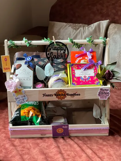 A two-tiered wooden stand hamper for Rakhi, decorated with an evil eye charm and stickers for a sister.