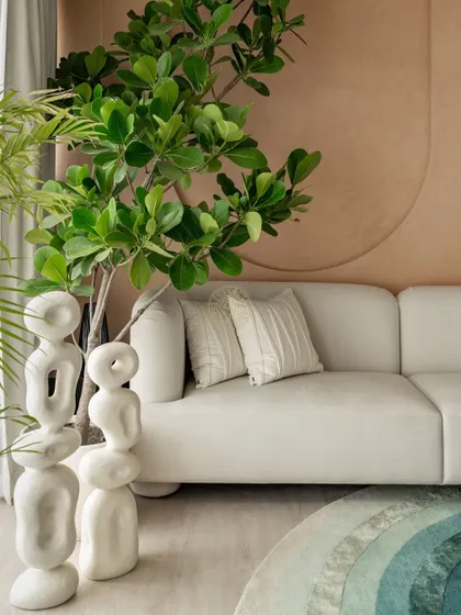 Detail shot of the living area, highlighting the clean lines of the white sofa next to abstract white sculptures. The wall behind features subtle, curved paneling that adds texture and depth to the neutral palette.
