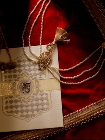 A detailed shot of a beautiful Sikh wedding invitation card featuring the 'Ek Onkar' symbol. This photo captures the cultural and personal touches that begin the wedding journey.