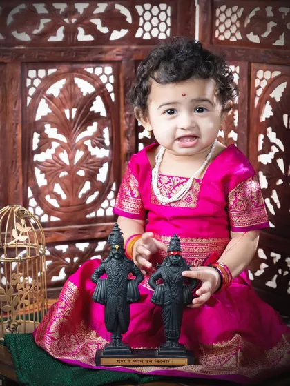 Another adorable shot from the Vitthal-themed sitter session. Her curious expression as she holds the small idols makes for a heartwarming and unique milestone portrait.