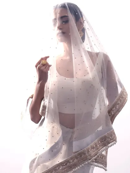 The sheer dupatta of the white organza saree, dotted with delicate sequins, creates a dreamy and romantic effect, perfect for a modern bride or a special occasion.