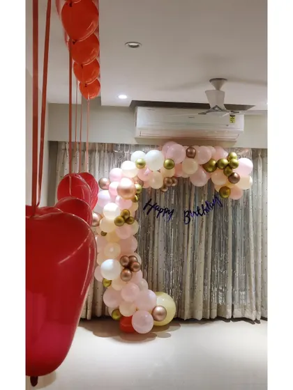A sophisticated decoration for a couple's birthday party at home, with a pastel and gold balloon arch and hanging heart balloons.