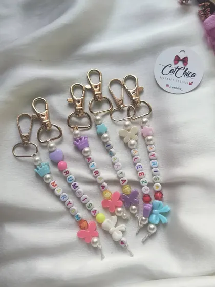 A close-up of the beautiful beaded name keychains we make for girls, featuring pearls and charms like crowns and butterflies.