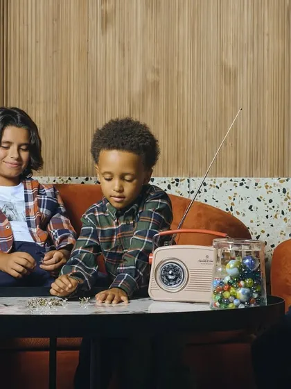 A lifestyle shot for a kids' fall collection. The warm tones, plaid shirts, and retro props create a cozy, nostalgic atmosphere.