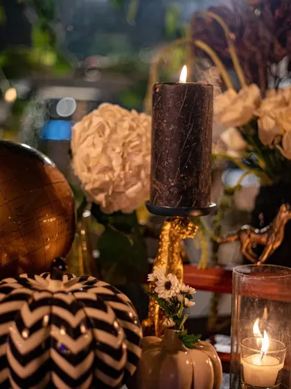 A black pillar candle stands on a golden holder, surrounded by whimsical decor elements like a chevron-patterned pumpkin. This image showcases our playful yet sophisticated approach to event styling.