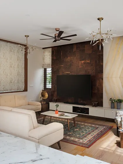 The living room's design incorporates a rich material palette, including a dark textured TV wall panel and a backlit onyx marble accent. These elements are balanced by the natural light and greenery from the adjacent courtyard.