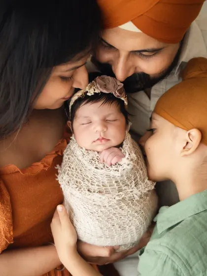 A beautiful family of four, with mom, dad, and big brother all kissing the new baby. A portrait overflowing with love.