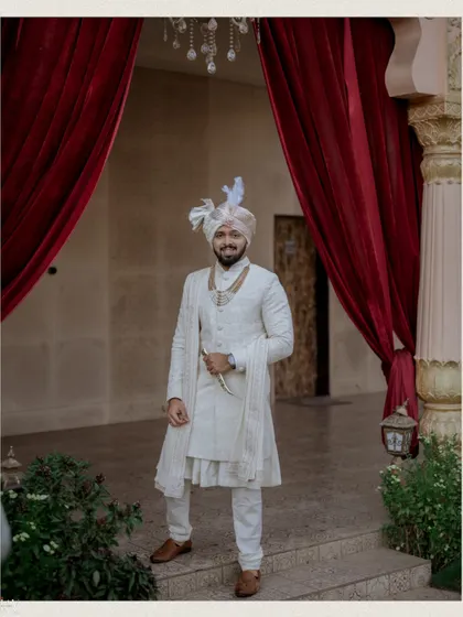 A full-length portrait of the groom in his classic white sherwani and turban.