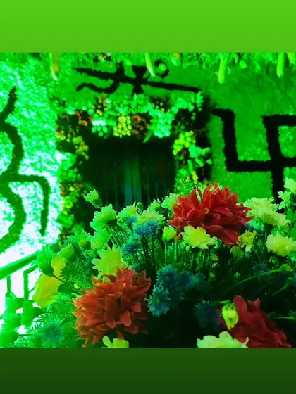 Sacred symbols like Om and Swastik created with flowers as part of a larger green floral backdrop, lit for effect.