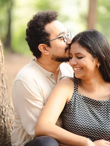 A warm, color portrait of Soham giving Anjum a gentle kiss on the forehead. The natural setting and their relaxed expressions make this a sweet and timeless image.