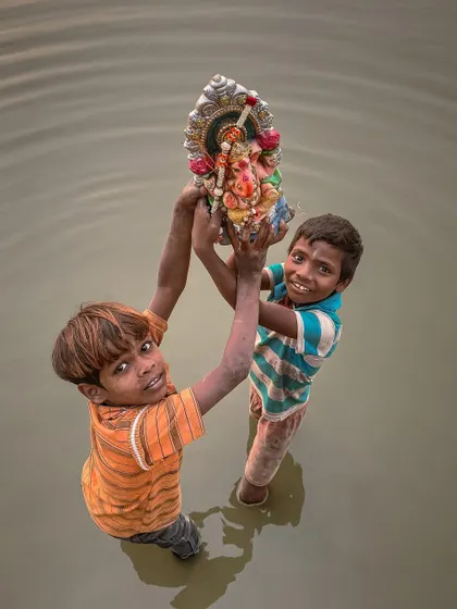 Two young boys rescue a small Ganesha idol from the water after the Visarjan, their faces a mix of determination and joy.