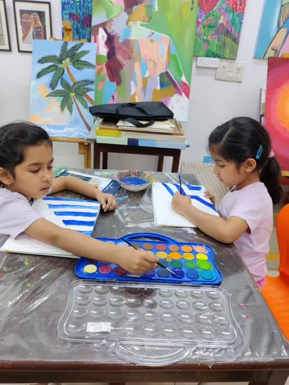 Two young sisters sit side-by-side, focused on their watercolor paintings. Art is a wonderful activity for siblings to share.
