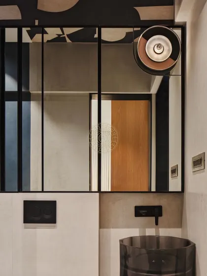 This bathroom uses a darker, more dramatic theme with a black-framed mirror, a smoked glass basin, and a unique ceiling light fixture. The design is modern, clean, and bold.