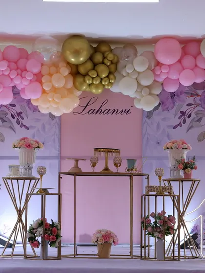 This elegant party setup features a pastel and gold balloon arrangement, a custom backdrop, and a coordinated set of dessert tables and plinths, suitable for first birthdays or baby showers.