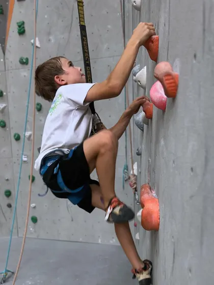 A young boy carefully navigates a route, demonstrating the focus and problem solving that climbing teaches.