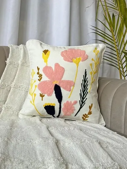 A beautiful floral embroidered boho cushion cover, styled on a sofa. The mix of pink and yellow flowers on a neutral base adds a soft, feminine touch.