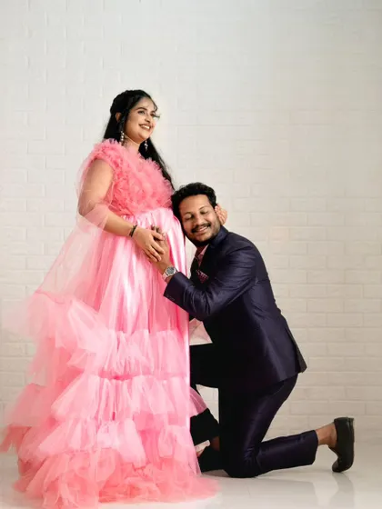 A heartwarming moment between partners during their maternity shoot. The pink gown and dark suit combination is a popular rental choice for couples.