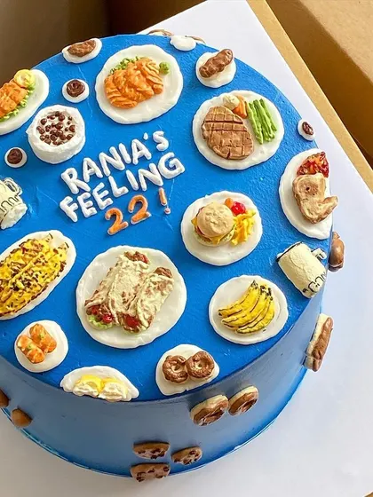A "Feeling 22" birthday cake covered in a variety of favorite foods, from tacos and burgers to corn on the cob, all in miniature edible form.