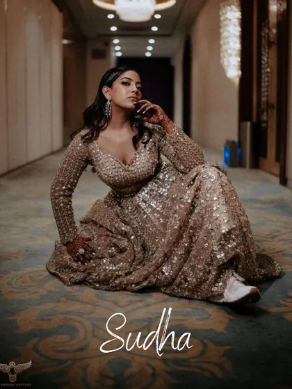 A full-length portrait with a modern, editorial feel. The bride is seated on the floor of a hotel corridor, looking confidently at the camera, her name elegantly watermarked on the image.