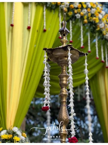 A detail shot of the traditional brass lamp, adorned with flowers, against the backdrop of the green and yellow mandap. It's these small touches that bring a sense of sacredness to the celebration.