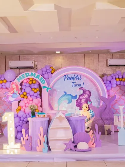 A full view of the mermaid-themed stage for a first birthday, complete with a ship, treasure chest, and beloved characters.