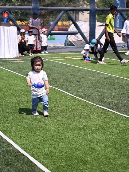 Another toddler confidently carries her ball and scoop across the field.