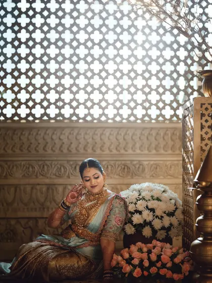 A bride seated amidst flowers, with beautiful light filtering through a traditional jali screen behind her. This portrait is full of grace, light, and intricate detail.