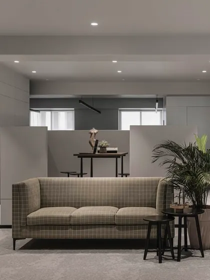 The waiting area features a checkered couch and nested side tables, offering comfort and style. A half-wall behind it creates a semi-open meeting nook, enhancing the office's flow while providing zones for privacy.