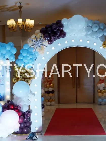 A welcoming entrance arch for a teddy bear party, decorated with blue, white, and gold balloons and a personalized photo of the birthday boy.