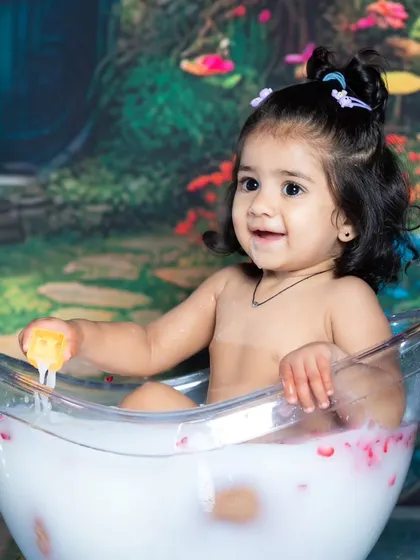 A happy baby girl enjoying her milk bath with rose petals.