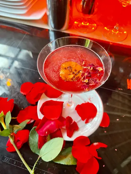 A romantic cocktail perfect for weddings or Valentine's Day. This deep red drink is garnished with edible rose petals and served on a plate scattered with fresh petals.